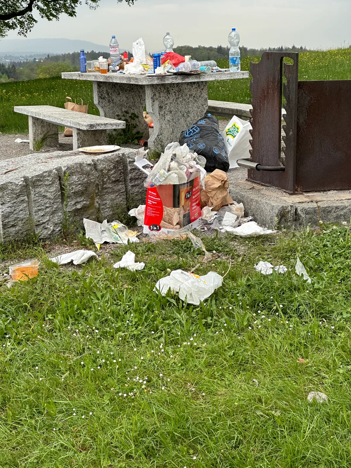 Man sieht diversen Abfall rund um eine Grill- und Feuerstelle.